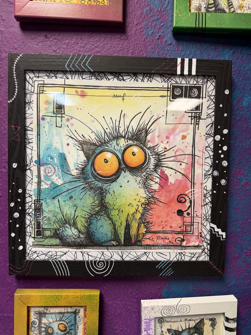 Framed creepy-cute watercolor creature by XZanthia, photographed against her painted gallery wall (piece 5 of 24)