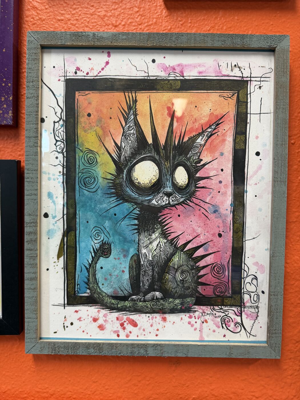 Framed creepy-cute watercolor creature by XZanthia, photographed against her painted gallery wall (piece 13 of 24)