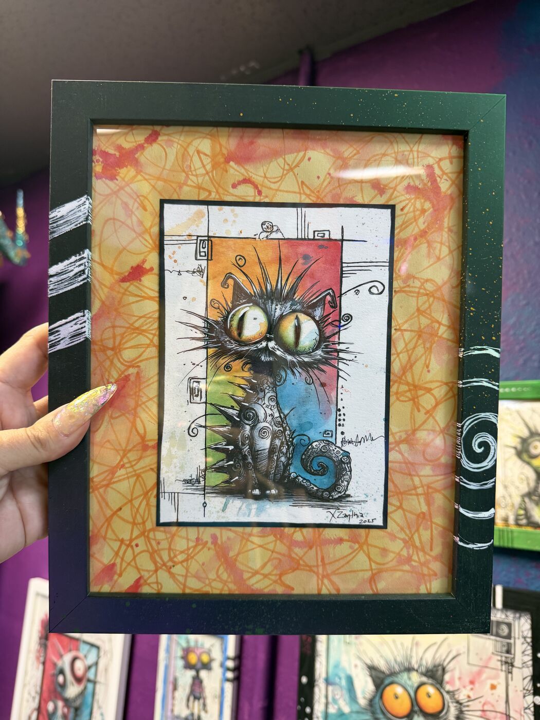 Framed creepy-cute watercolor creature by XZanthia, photographed against her painted gallery wall (piece 14 of 24)