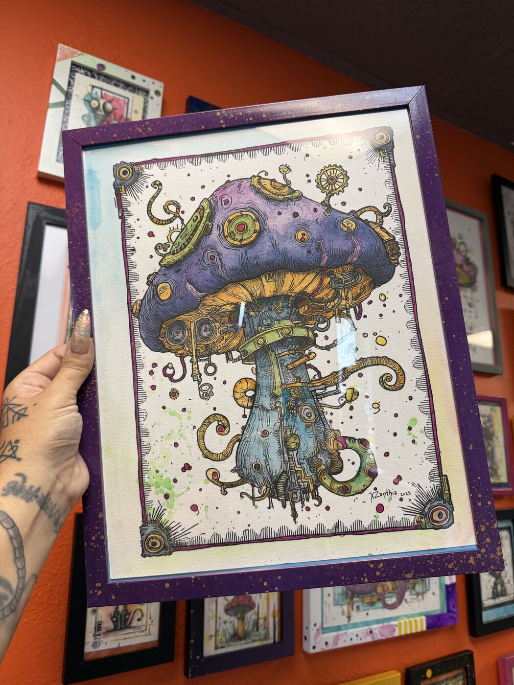 XZanthia holding a framed purple mushroom watercolor in her studio