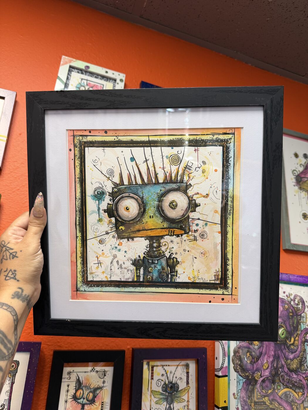 Framed creepy-cute watercolor creature by XZanthia, photographed against her painted gallery wall (piece 21 of 24)