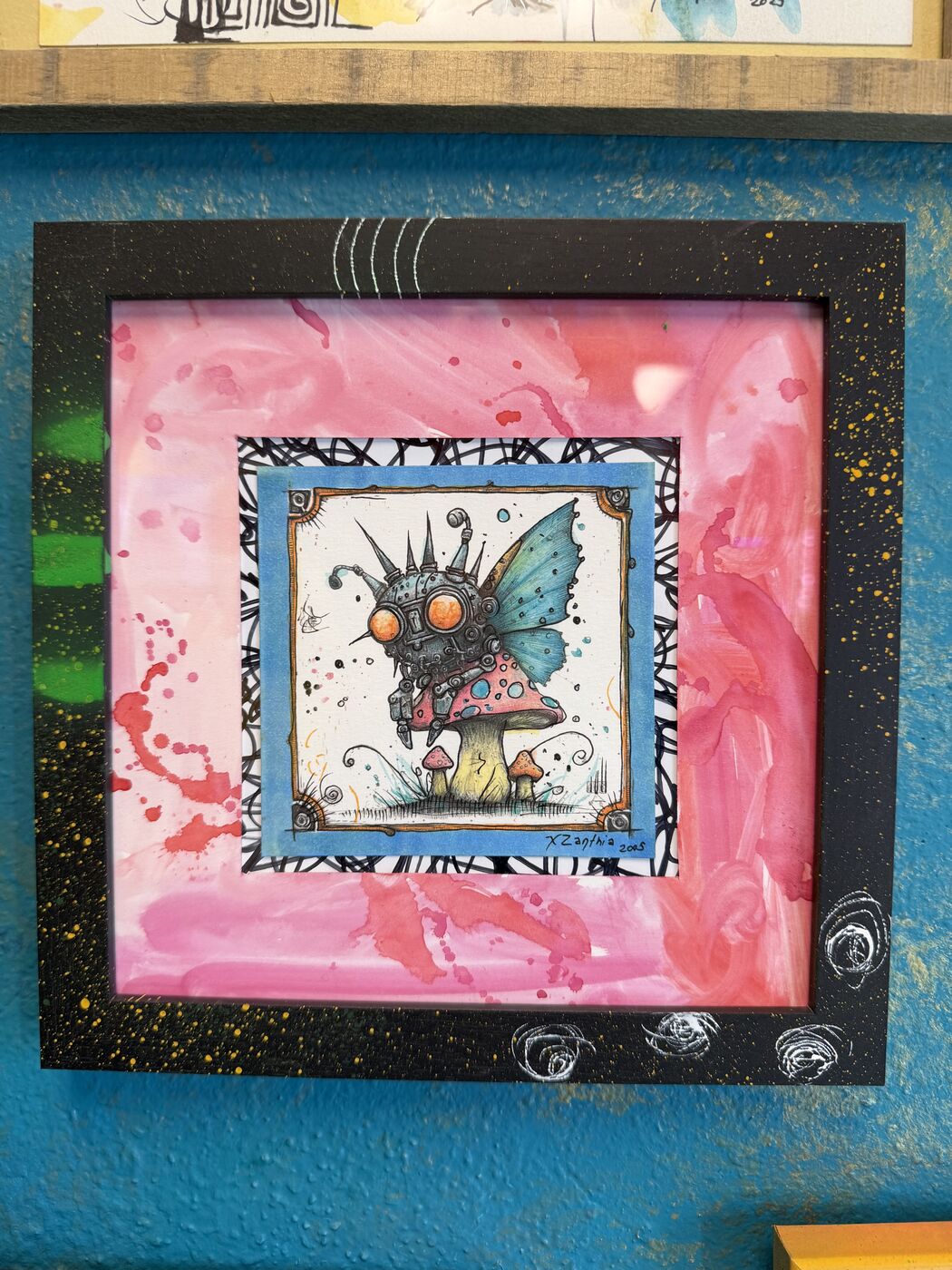 Framed creepy-cute watercolor creature by XZanthia, photographed against her painted gallery wall (piece 22 of 24)