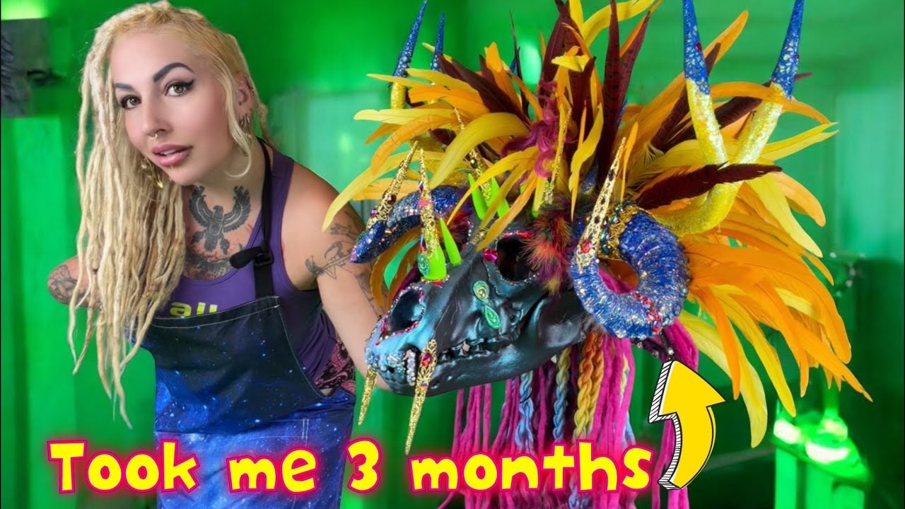 XZanthia in her apron beside a huge rainbow-feathered tribal mask she sculpted